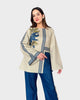 Woman wearing a beige top with floral embroidery and blue pants on a white background