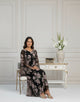 Woman in a floral dress sitting in a elegant room with a vase of flowers on a table.